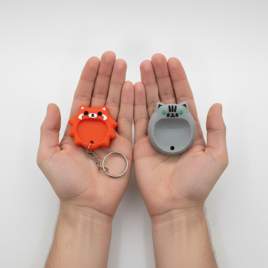 Dos manos sosteniendo dos Worry Stones con diseño de animales: uno naranja con forma de zorro y otro gris con forma de gato, ambos de tamaño pequeño y pensados como objetos antiestrés y de relajación táctil.